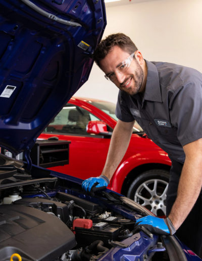 Express Care employee smiling while looking under hood of car